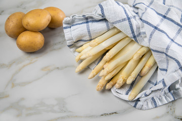 Roher, weißer Spargel in Tuch und Kartoffeln auf Marmor Hintergrund