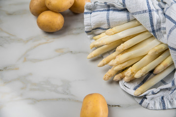 Roher, weißer Spargel in Tuch und Kartoffeln auf Marmor Hintergrund