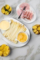 Platte weißer Spargel mit Sauce Hollandaise, zerlassener Butter, Kochschinken, geräucherten Schinken und Kartoffeln auf Marmor Hintergrund