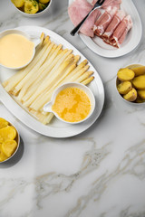 Platte weißer Spargel mit Sauce Hollandaise, zerlassener Butter, Kochschinken, geräucherten Schinken und Kartoffeln auf Marmor Hintergrund