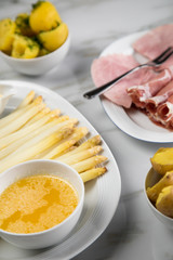 Platte weißer Spargel mit Sauce Hollandaise, zerlassener Butter, Kochschinken, geräucherten Schinken und Kartoffeln auf Marmor Hintergrund
