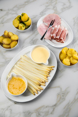 Platte weißer Spargel mit Sauce Hollandaise, zerlassener Butter, Kochschinken, geräucherten Schinken und Kartoffeln auf Marmor Hintergrund