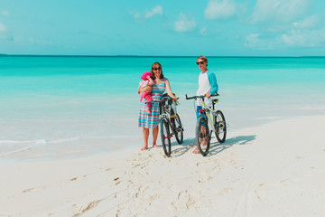 Fototapeta premium happy young family with baby riding bikes on beach