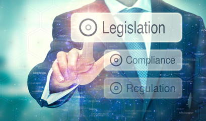 A business man selecting a button on a futuristic display with a Legislation concept written on it.