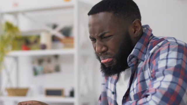 Black man feeling unpleasant taste and smell eating dinner, spoiled food, gmo