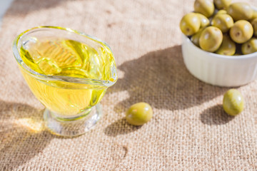 fresh marinated green olives in white ceramic bowl and sauceboat of premium virgin olive oil  on  burlap cloth background