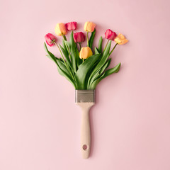 Creative spring concept made with paint brush and colorful tulip flowers on pastel pink background....