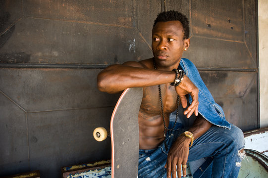 young handsome and attractive black African American skateboarder man sitting on city grunge bench holding skate board posing in cool attitude
