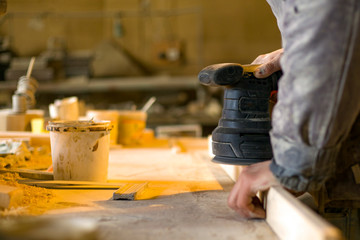 Carpenter works in the workshop of processing wooden boards, grinding machine, sander in the hands of a worker