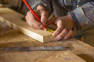 measuring with a centimeter and a pencil by a carpenter in a woodworking workshop