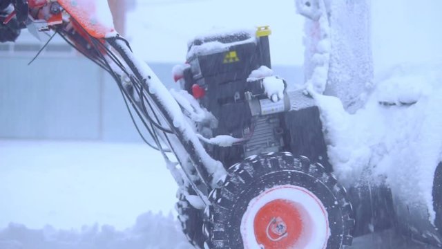 The man is removing snow with a snow blower in a blizzard. Slow motion.