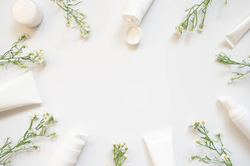 Skin​care​ packaging​​ set w/ spring flowers on​ white​ background.​ Natural beauty​ cosmetology​ concept.​ Copy​ space​ for​ text or​ mock-up​ cosmetic​ branding​ products.​ Top​ view. Flat lay.