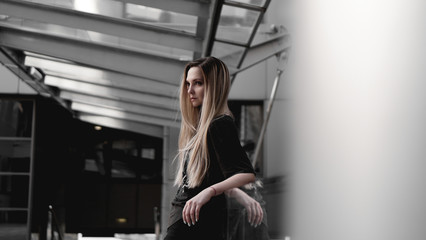 Urban style blonde girl with a stern look standing on the background of a modern building. Wearing black shirt. Girl power and subculture concept.