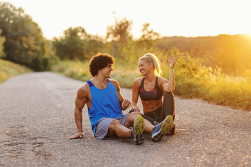 Smiling beautiful sporty couple in love sitting on the country road and resting on sunny summer day.