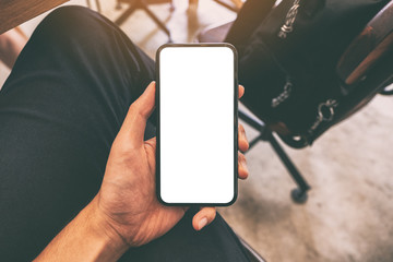 Mockup image of a man's hand holding black mobile phone with blank screen with a cup of coffee on the table in cafe