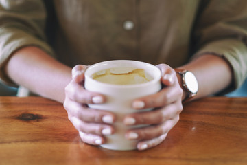 Closeup image of woman's hands holding a cup of hot coffee on wooden table