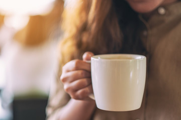 Closeup image of a woman holding a white cup of hot coffee