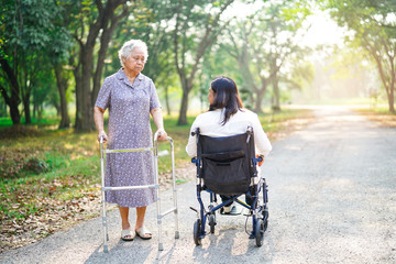 Asian senior or elderly old lady woman patient walk with walker greet middle age friend on wheelchair in park : healthy strong medical concept 