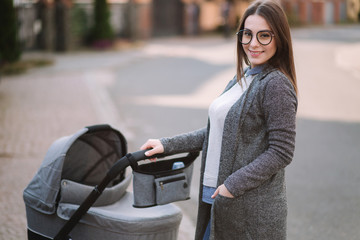 Family, child and parenthood concept - Happy mother with stroller in the park. Mom with sunglasses and stylish grey jacket