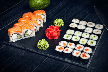 Set of sushi rolls with salmon on dark stone served with ginger and wasabi and wooden black wooden table. Fresh Japanese cuisine. Close up view on asian food. Sushi image for menu.