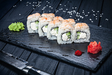 Close up view on sushi rolls Philadelphia with shrimp on dark stone served with ginger and wasabi and wooden black wooden table. Fresh Japanese cuisine. Copy space. Served sushi for menu