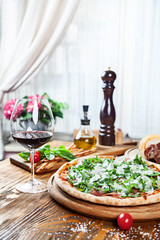 Close up view on fresh served pizza with prosciutto on a wooden table on light background. Pizza with wine. Vertical image with copy space for text. Food for menu. Italian cuisine. 
