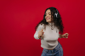 Beautiful smiling girl, with headphones, dancing and listening to music with closed eyes, all over a red background 