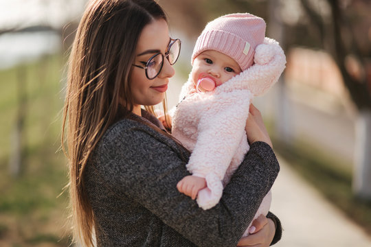 Portrait of mother and her little baby girl. Beautiful mom and cute baby. Mother hud her daughter. Baby dressed in peanch colour hat and nipple toy