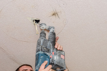 A man holds a power drill in his hands. Make a hole in the ceiling. Repair work in the apartment....