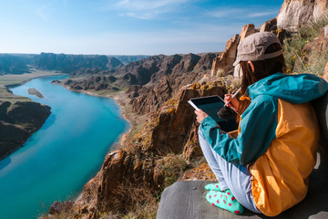 The girl draws the spring landscape of the river on the graphics tablet