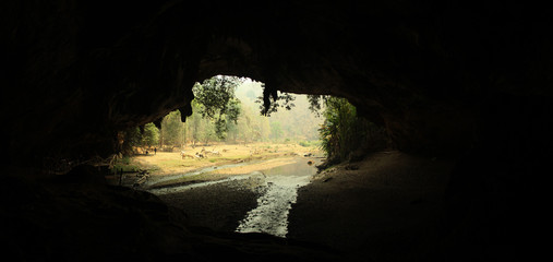 wide angle panoramic view showing the opening of a cave, Thum Lod cave, Bang Ma Pha, in Northern Thailand. Touristed cave with stalagmites and stalactites and a river running thru it.