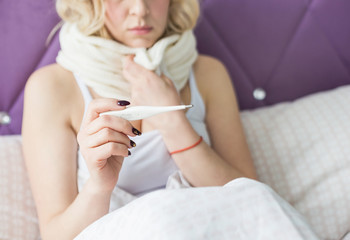 Obraz na płótnie Canvas Beautiful blond woman sitting in bed with a thermometer and a scarf wrapped around the neck and a handkerchief. illness and health at home