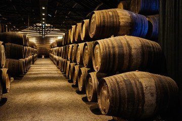 Old aged traditional wooden barrels with wine in a vault lined up in cool and dark cellar in Italy, Porto, Portugal, France