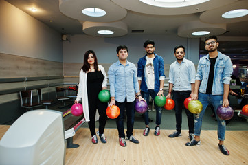 Group of five south asian peoples having rest and fun at bowling club. Holding bowling balls at hands.