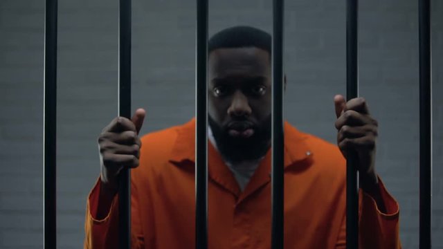 African-american male prisoner holding bars and looking to camera, imprisonment