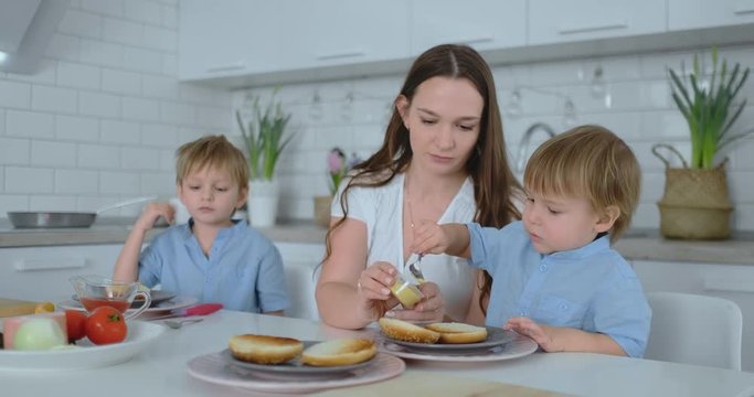 Beautiful young mother with two children sons on white light kuna cook with burgers