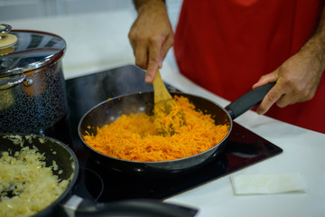 man chef cooks carrots and onions on an electric stove in a black frying pan