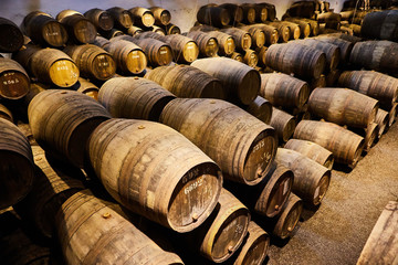 Old aged traditional wooden barrels with wine in a vault lined up in cool and dark cellar in Italy, Porto, Portugal, France