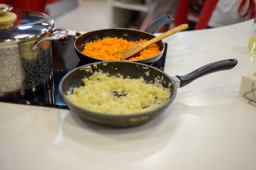 carrots and onions are fried or stewed on an electric stove in a black frying pan