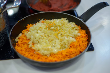 carrots and onions are fried or stewed on an electric stove in a black frying pan