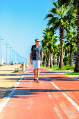 Young attractive guy walks along the pedestrian road with palm trees in the summer, near the Black Sea coast, Batumi, Georgia