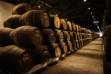 Old aged traditional wooden barrels with wine in a vault lined up in cool and dark cellar in Italy,...