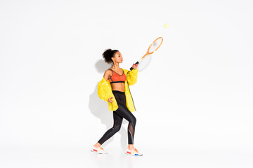 athletic african american sportswoman exercising with tennis racket and ball on white
