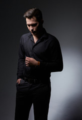 Fototapeta premium Thinking serious handsome sad business man looking down in black fashion shirt and jeans looking down on dark shadow background. Art.