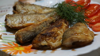 Fried fish smelt on a plate, served with tomatoes and dill.