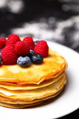 Closeup photo of plate of pancakes, blueberries, raspberries and powdered sugar.