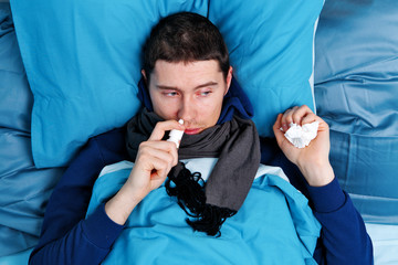 Sick brunet man using nasal spray while lying in bed