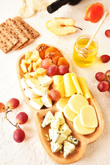 Cheese set on a plate laid out on a beige background. Different types of cheeses: Camembert, Parmesan, blue cheese, olives, honey, grapes.