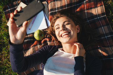 Fototapeta premium Cheerful teenage girl laying on a blanket at the park
