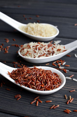 Different types of rice in spoons on wooden table background